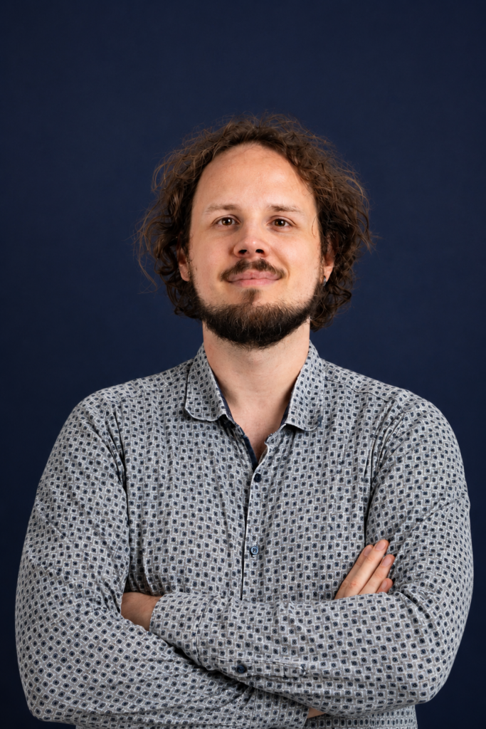 Benedict Krämer mit verschränkten Armen im grau karierten Hemd vor dunkelblauem Hintergrund