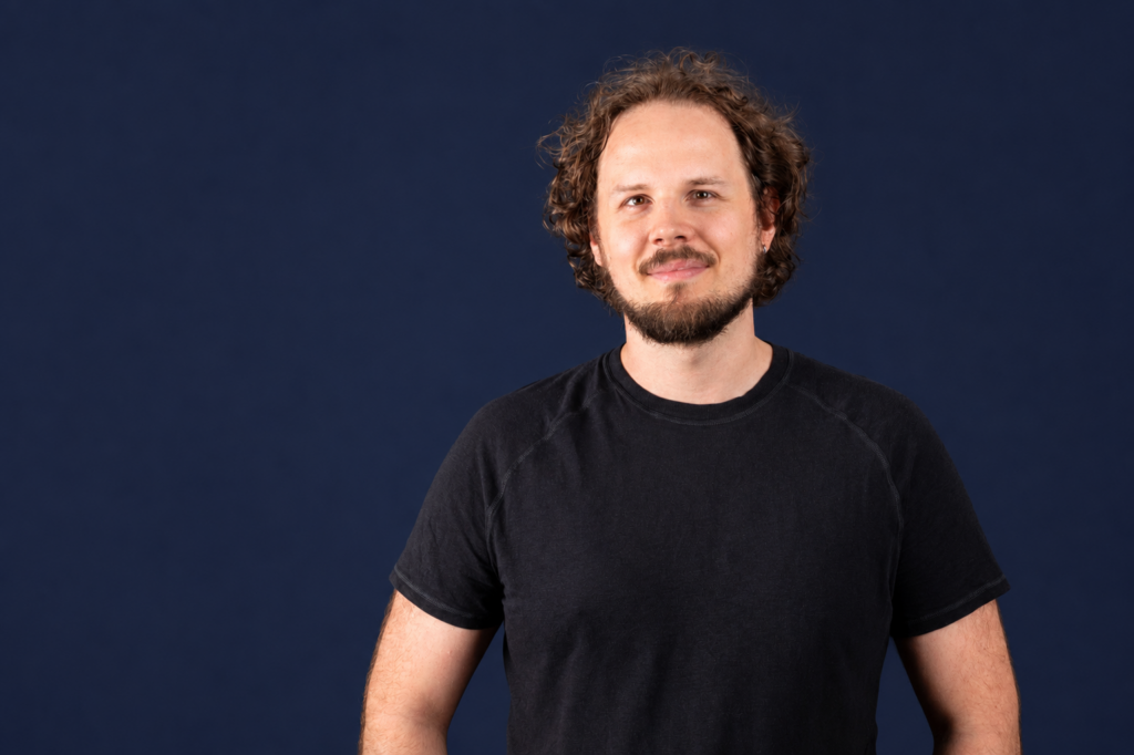 Benedict Krämer, lächelndes Porträt vor dunkelblauem Hintergrund
