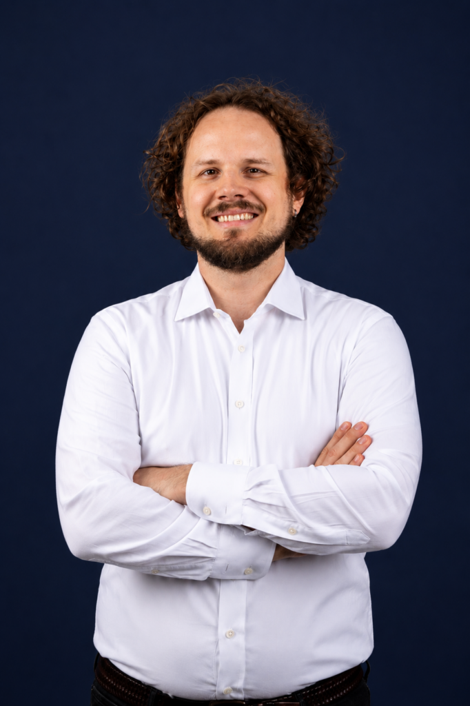 Benedict Krämer mit verschränkten Armen im weißen Hemd vor dunkelblauem Hintergrund